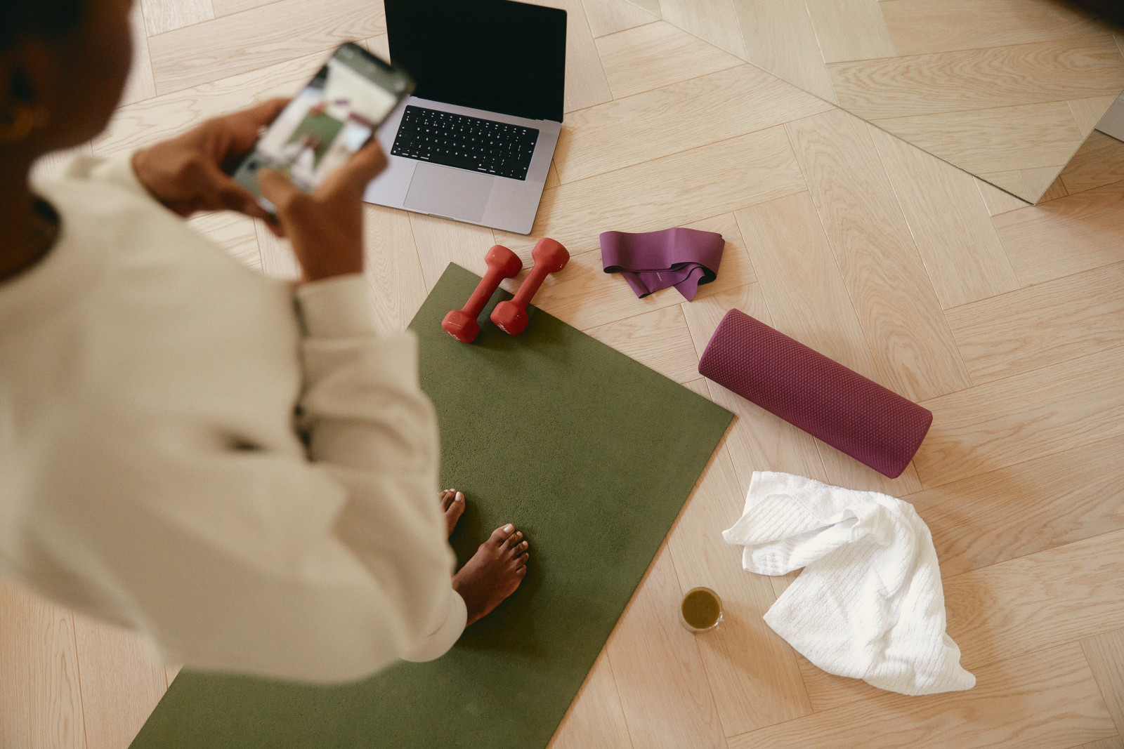 woman standing on yoga mat taking pictures of her weights, towel, and roller with computer in front of her